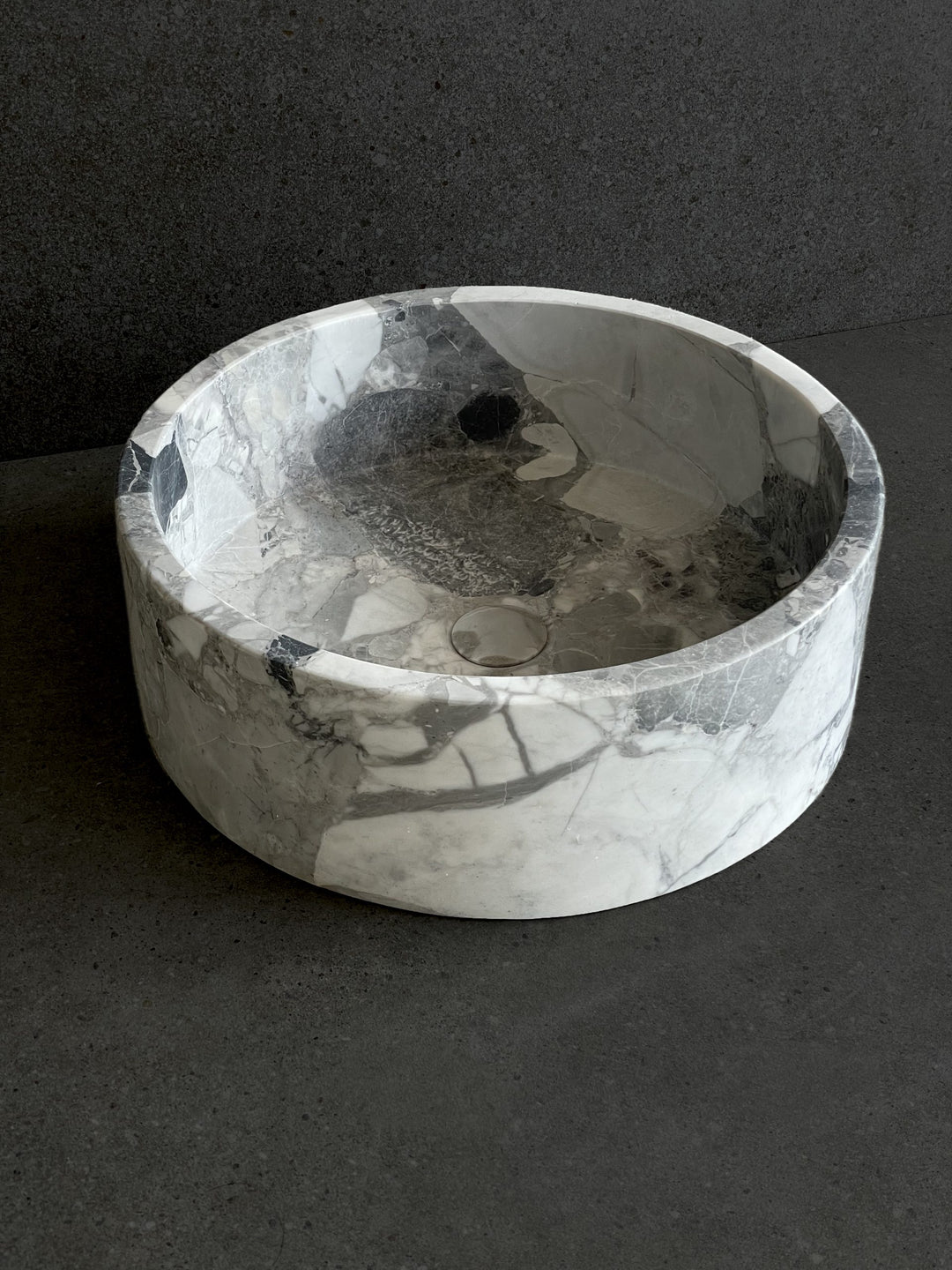 Round marble-look ceramic basin with smooth polished finish on dark surface