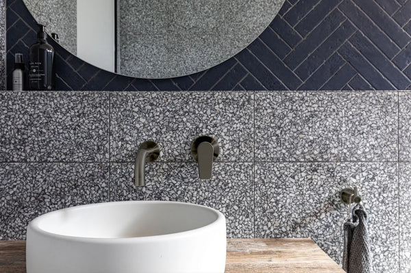 Wall-mounted mixer taps in dark finish installed above a freestanding basin with textured stone wall background