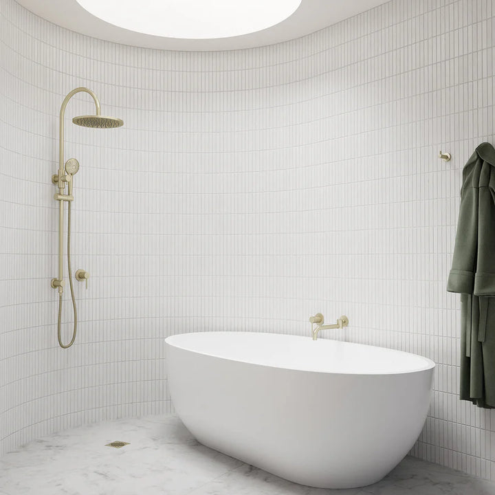 Freestanding white bathtub with gold shower system and wall-mounted shower head in modern tiled bathroom