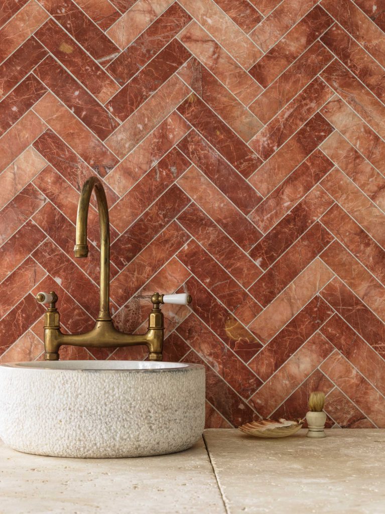 Brass wall-mounted tapware installed against terracotta herringbone tile backsplash