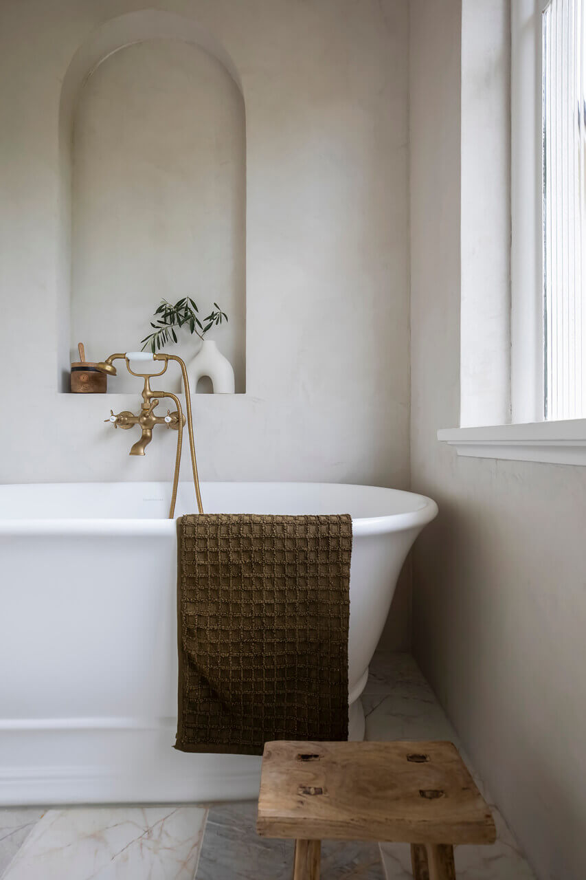 Bathroom with white freestanding bathtub, wooden stool, and green towel.